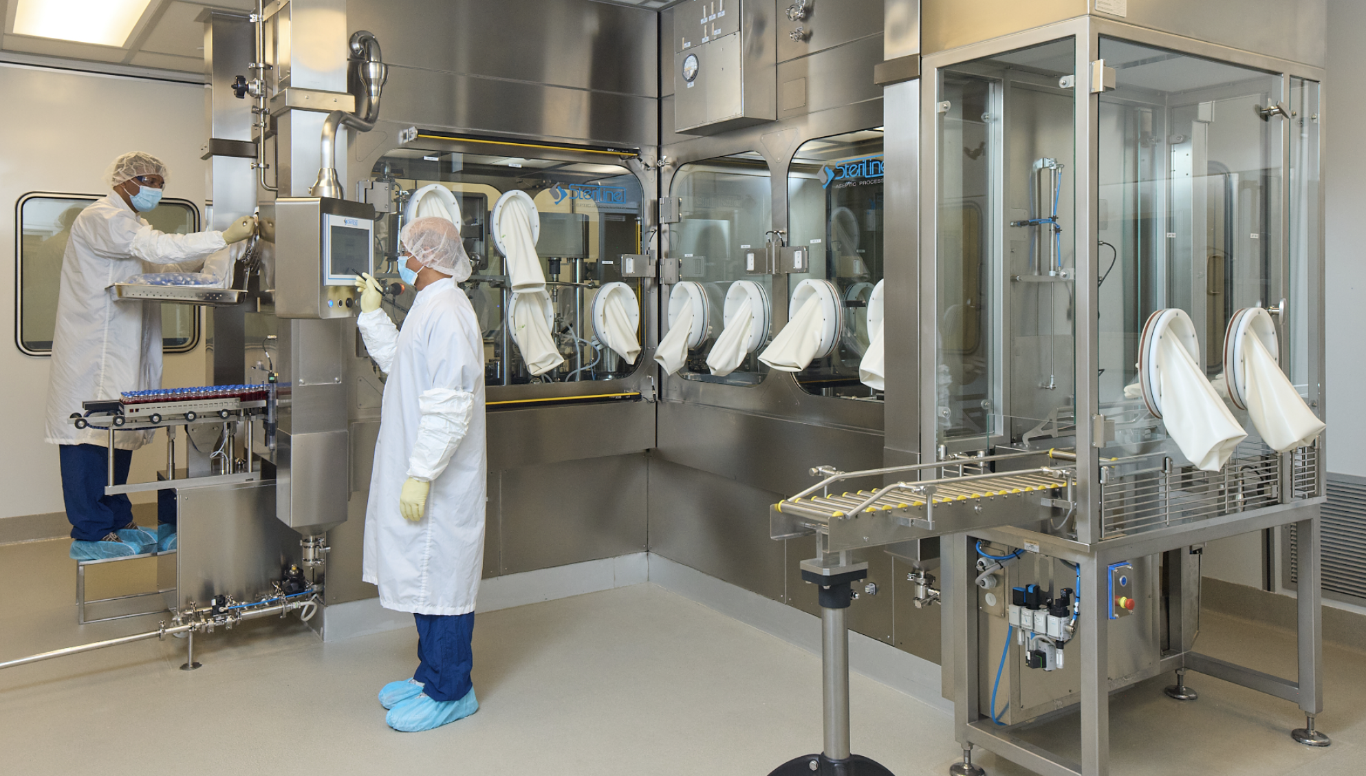 Two workers in white clean suits working on a large machine